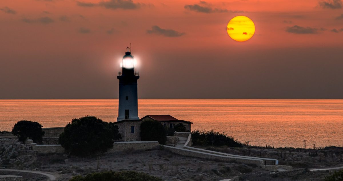 a lighthouse with a bright yellow sun in the background